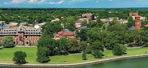 Aerial view of Hampton University, with water at the bottom of the image and prominent buildings and land at the top 90%